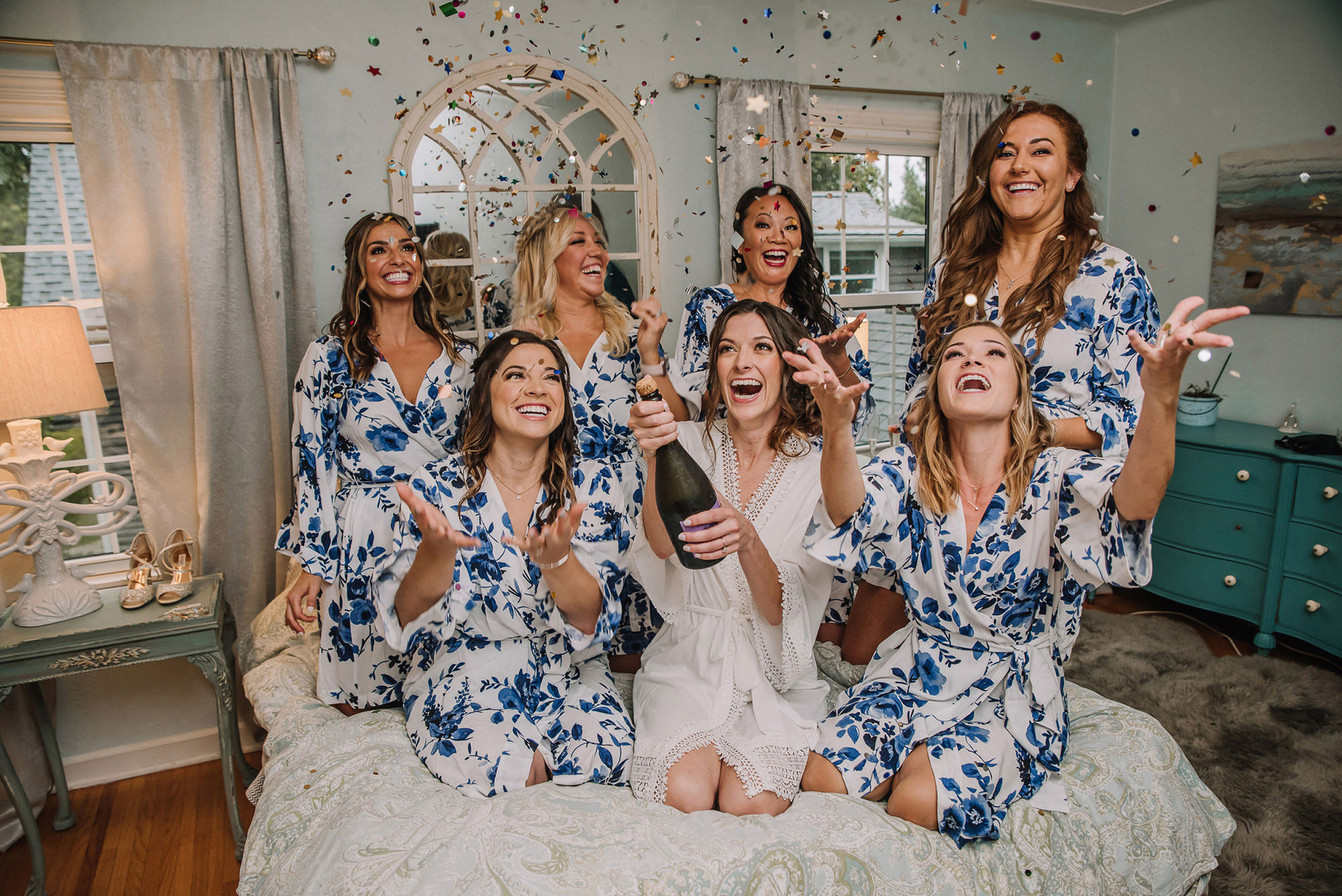 bridesmaids on bed tossing confetti with champagne